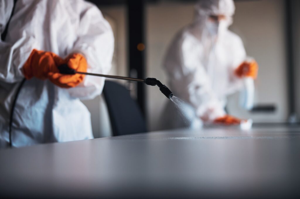 Janitorial workforce in hazmat suits sanitizing the office desks